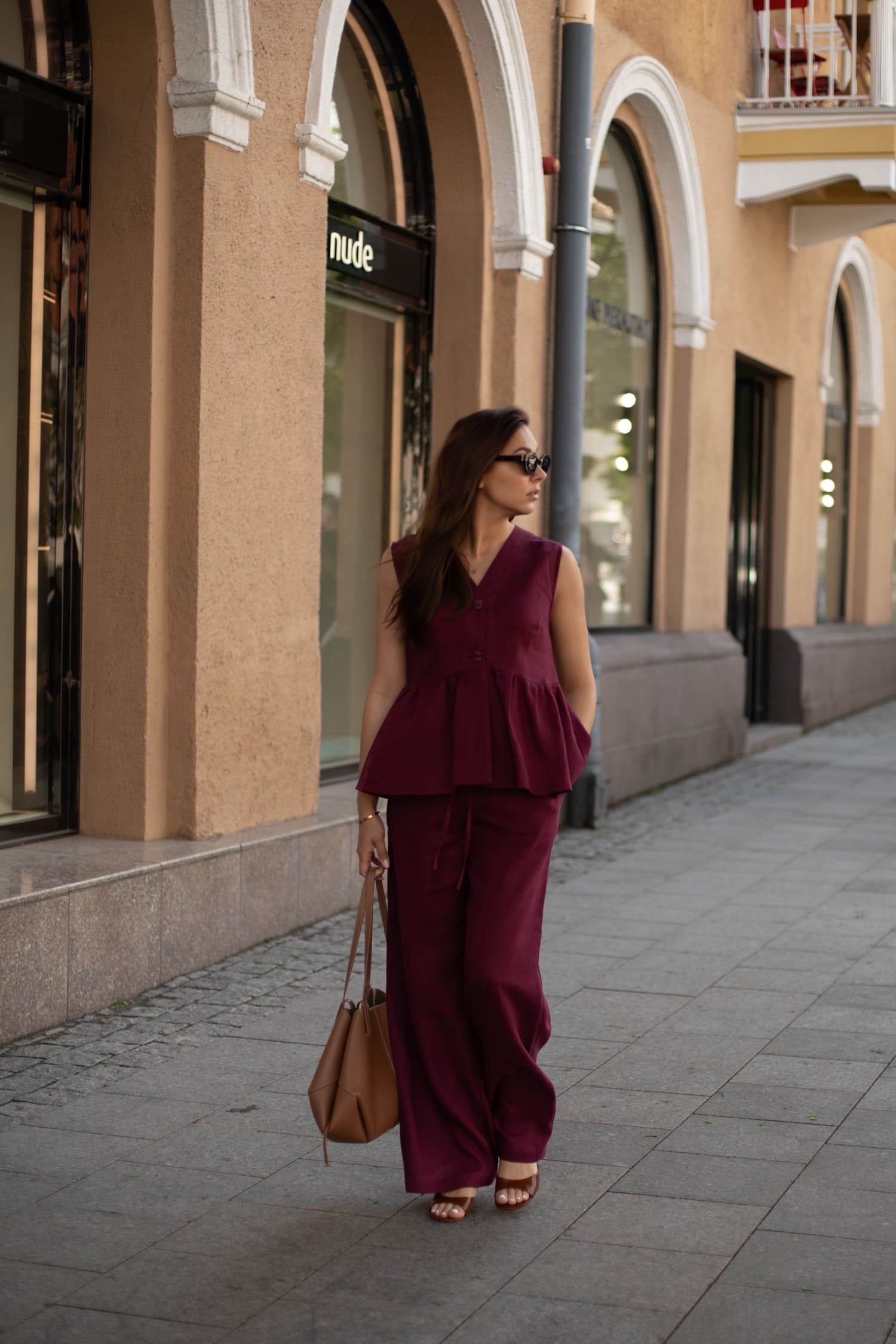 Moteris vilki bordo lininę peplum palaidinę ir plačias linines kelnes miesto aplinkoje